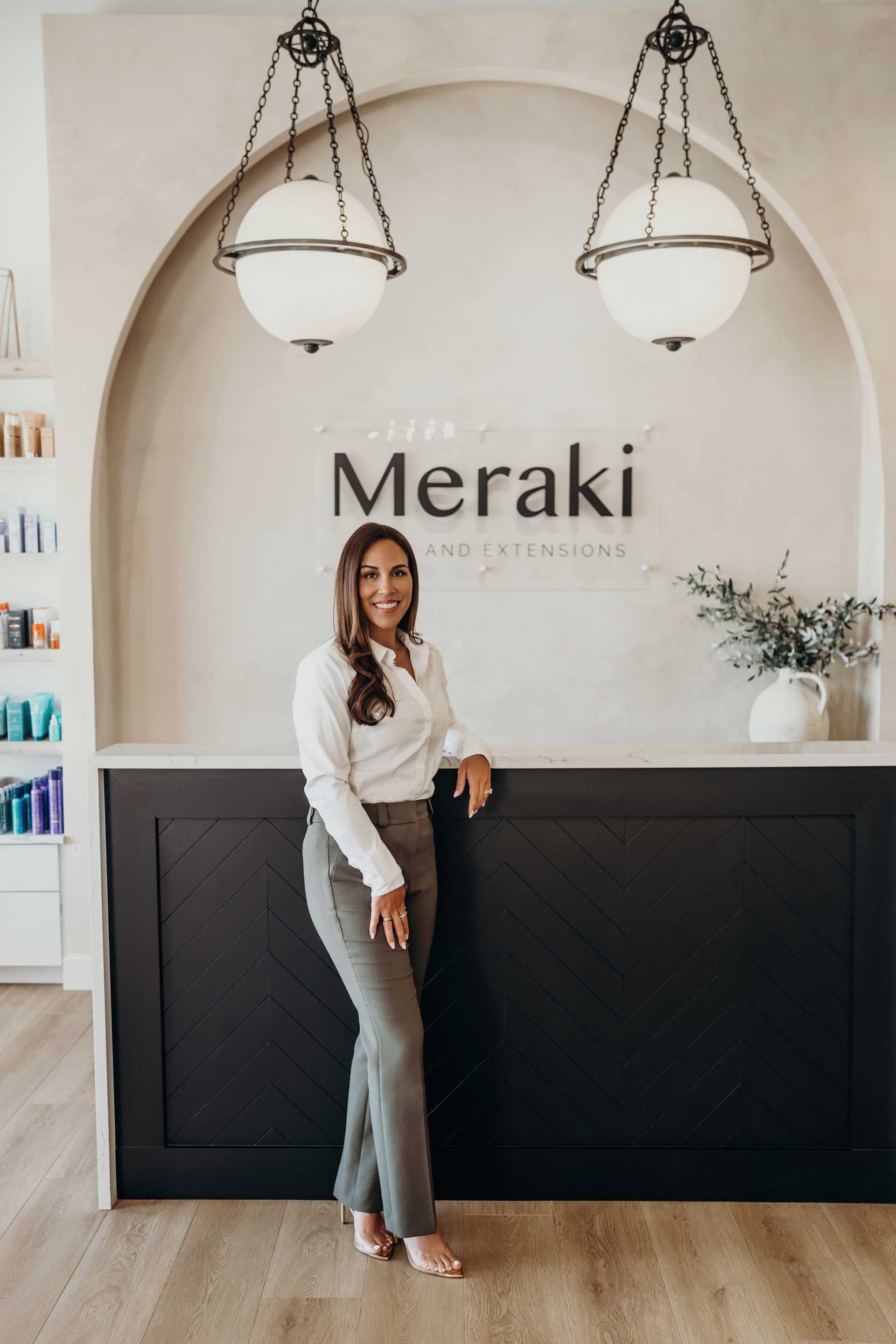 Woman standing at a salon reception desk with elegant decor and ambient lighting.