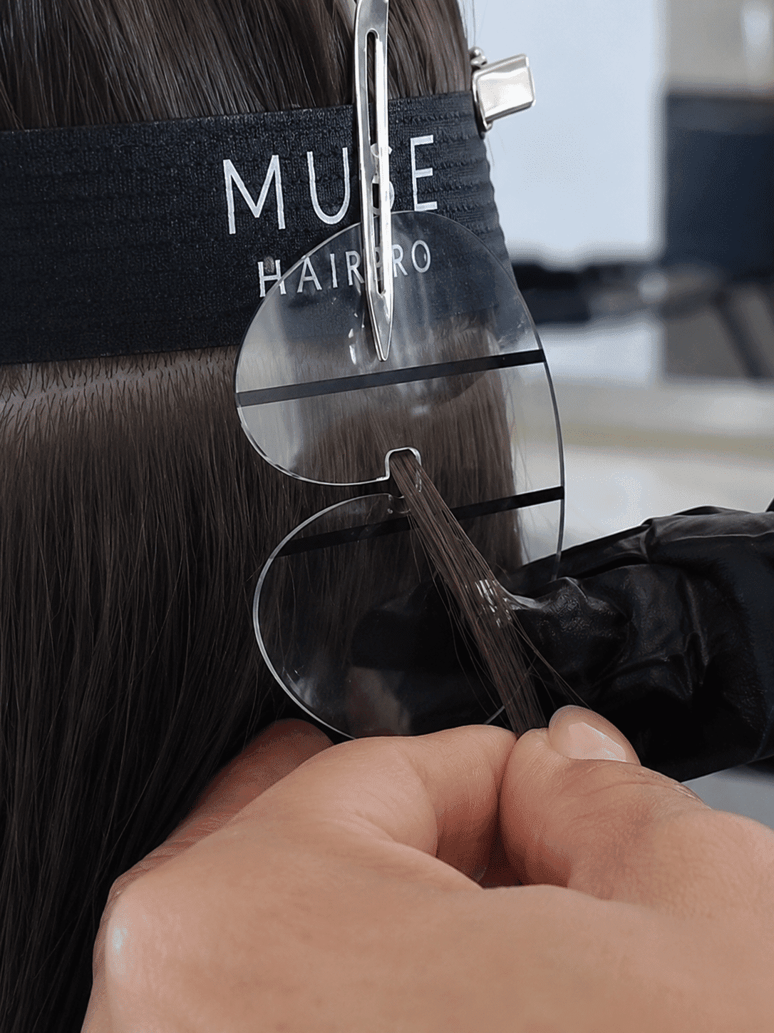 Hair stylist using a clear tool to dye strands of brown hair in a salon.
