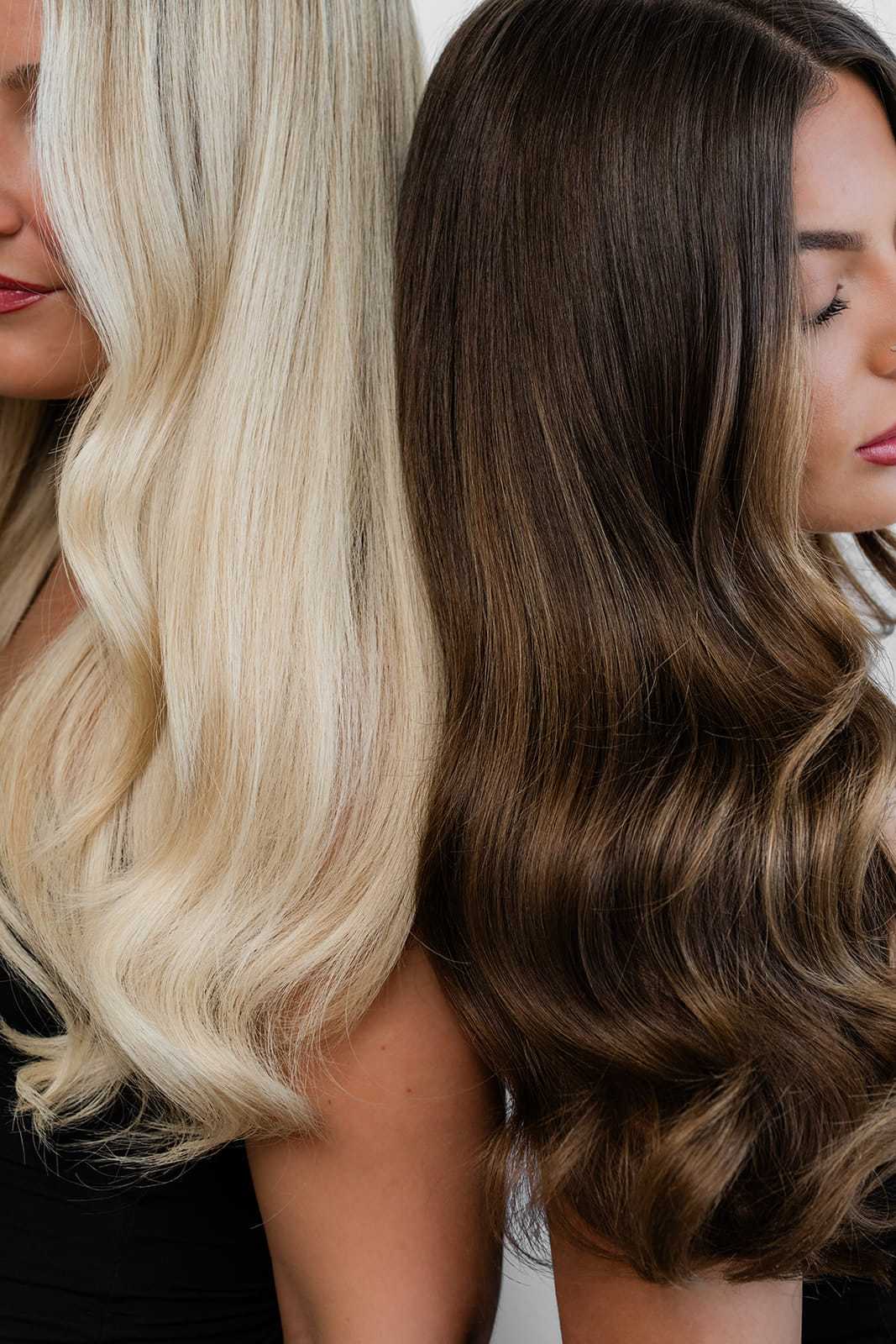 Two women with long, wavy hair. One has blonde hair, the other has brown hair.