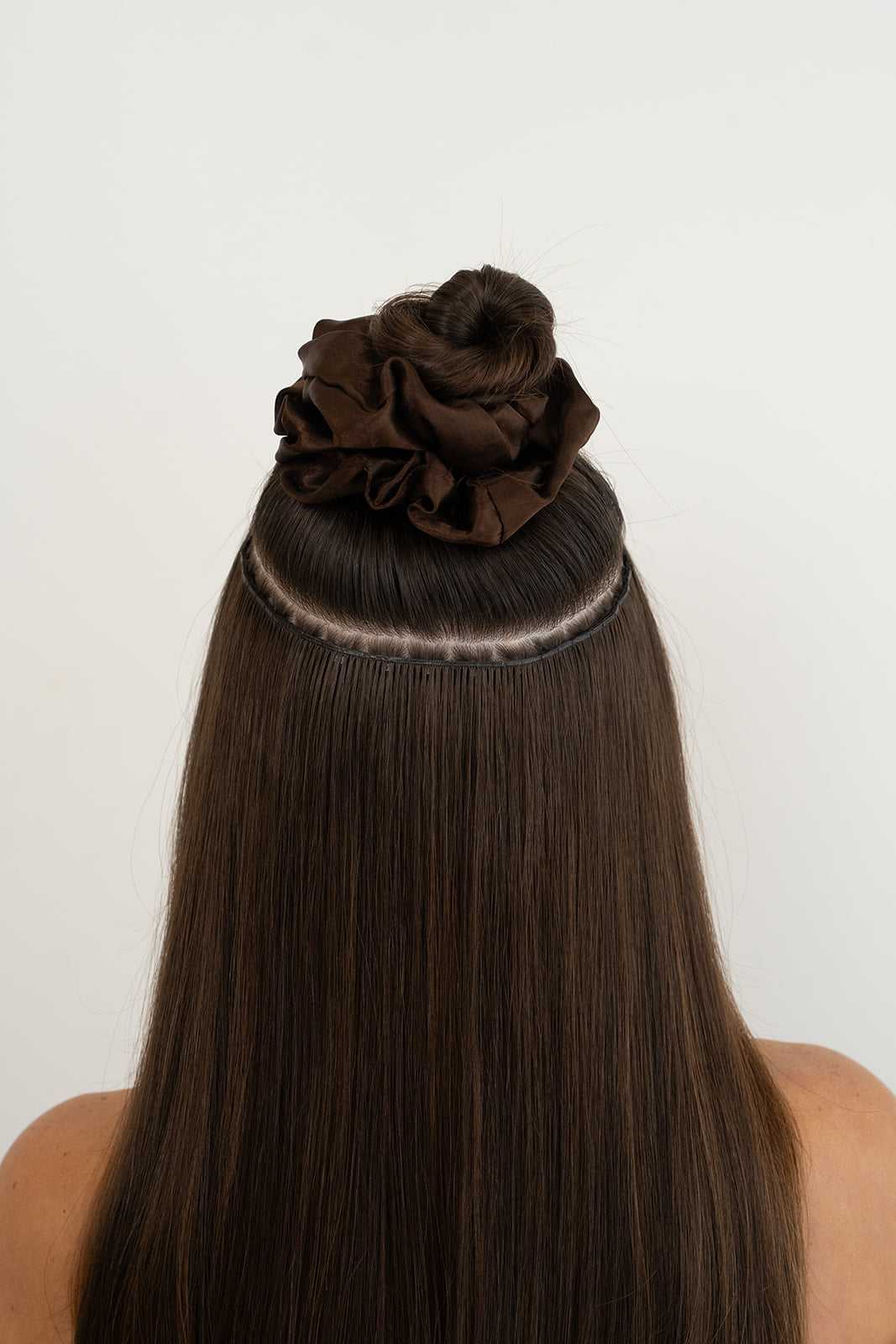 Close-up of brown hair extensions being applied to long hair, styled with a neat top bun.