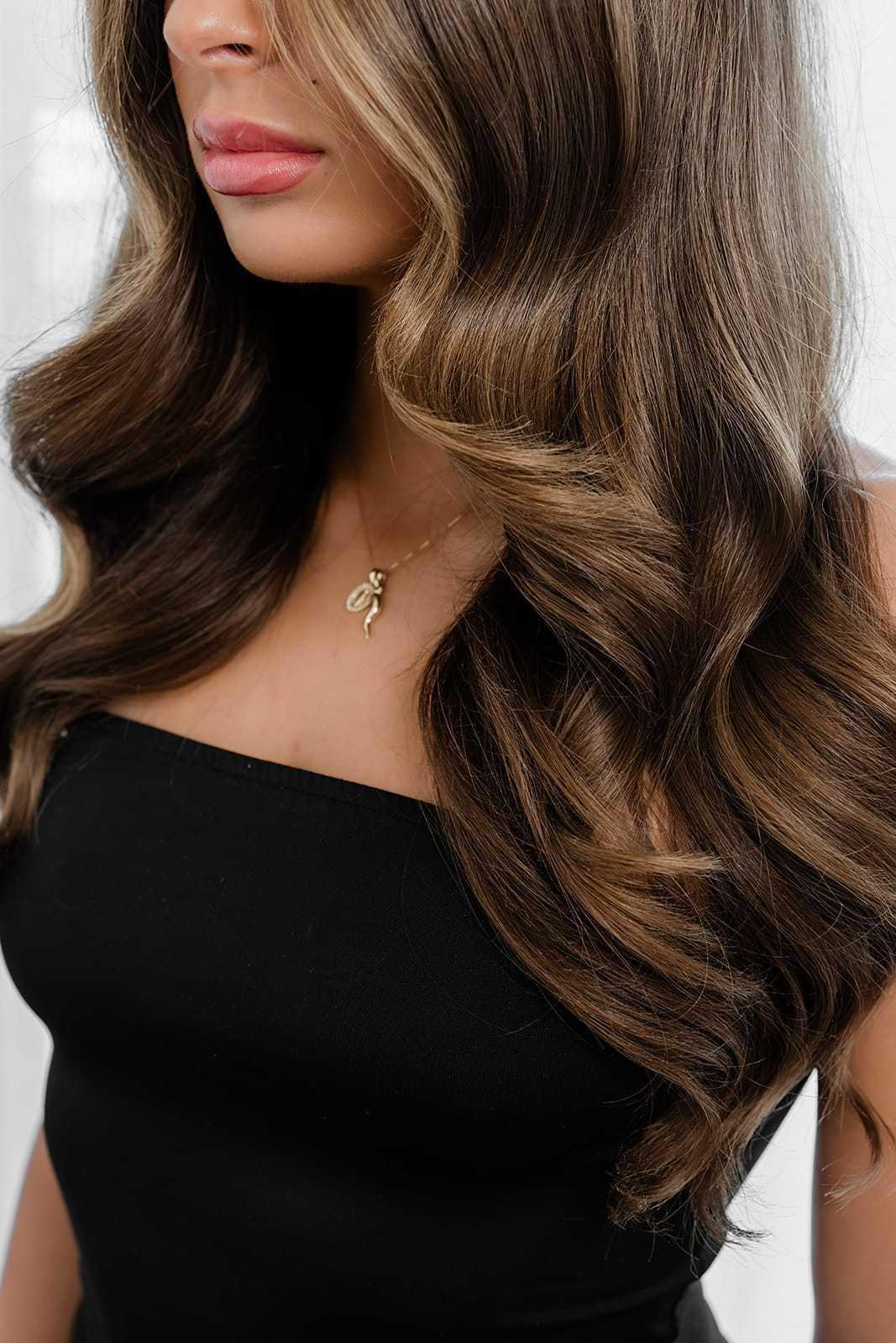 Long, wavy brown hair on a woman wearing a black strapless top, with a simple gold necklace.